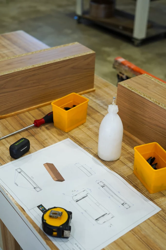 Plan technique, pièces de mobilier et outils de fabrication sur un établi de l'atelier Castany Agencement.